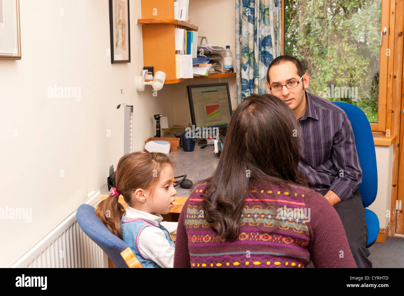 GP Doctor surgery patient consultation UK. Doctor seeing young child with her Mother in surgery. Stock Photo
