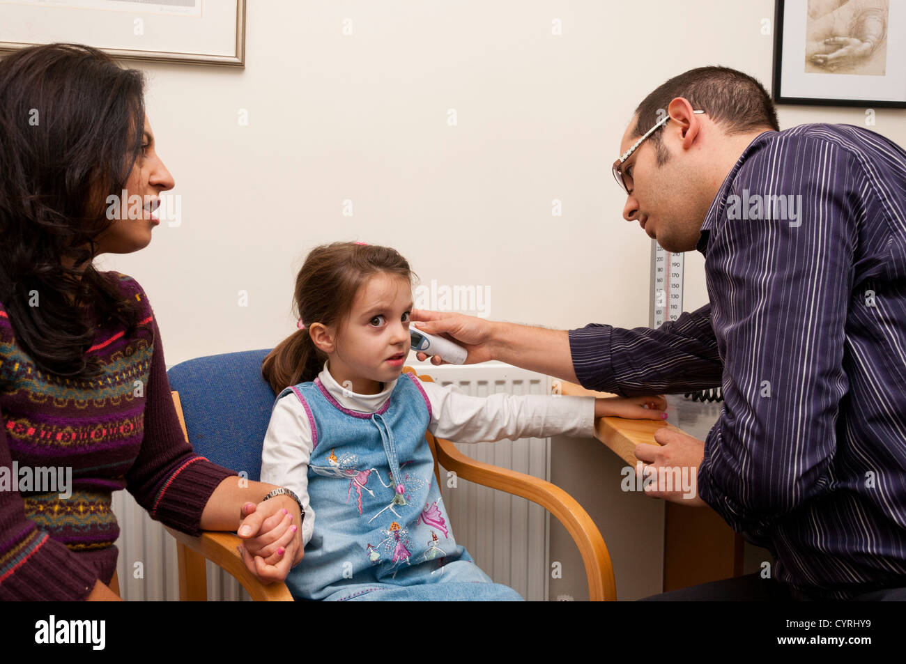 GP surgery patient consultation UK. Doctor checking temperature of a six year old girl. Stock Photo