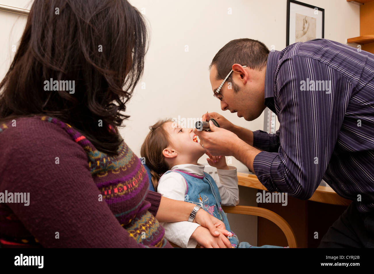 GP Doctor surgery patient consultation. Doctor examines throat of a young child while her Mother watches. UK Stock Photo