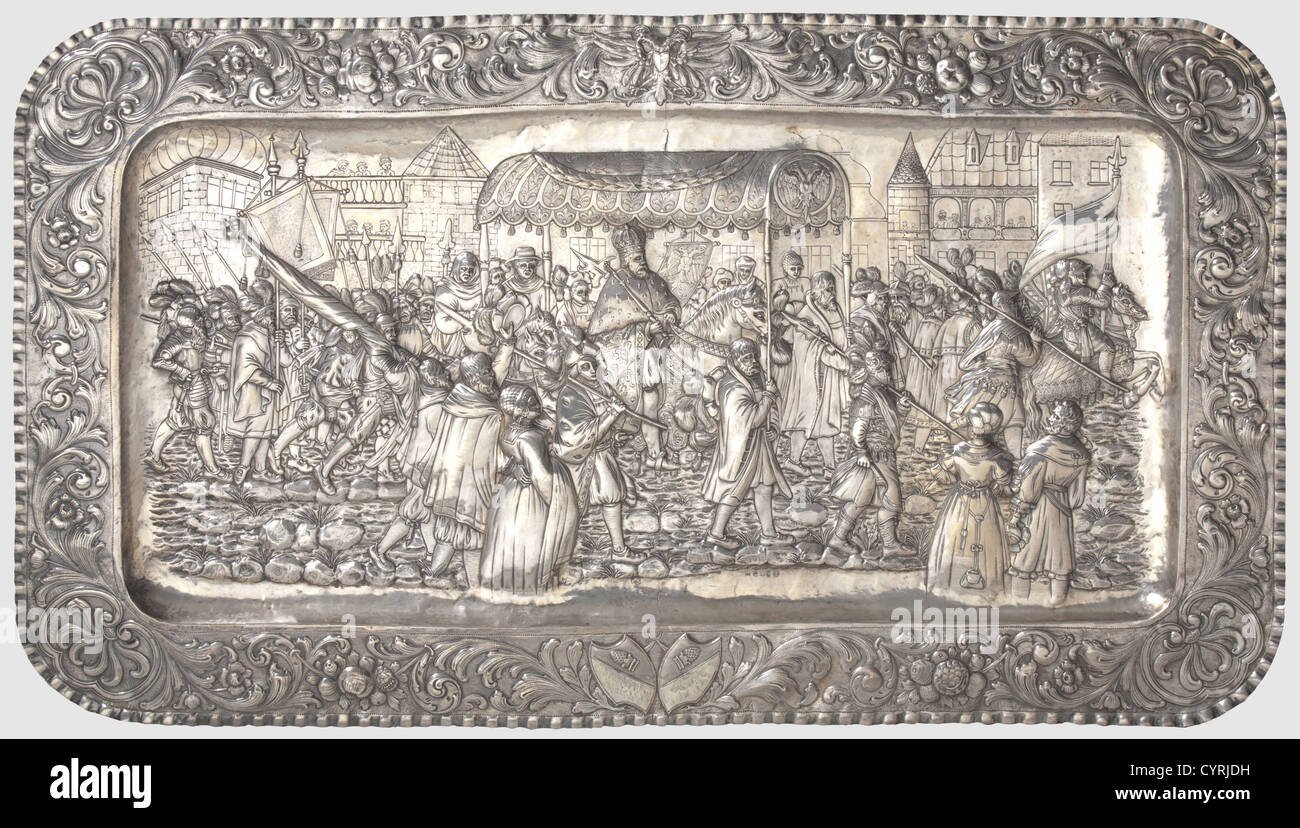 A large German silver memorial display platter, Emperor Charles V's entry into Augsburg for the 1548 Reichstag 2nd half of the 19th century Chased platter embossed in high relief with a figure staffage in front of house scenery. The floral decorated border displays a double-headed eagle as the imperial coat of arms and the double coat of arms for the city of Augsburg. A '930' hallmark, an eagle mark for Bruckmann Heilbronn, and the city marks for Augsburg, the Pyr, a striding lion, and a portrait head in the centre of the reverse side. Dimensions 119 , Artist's Copyright has not to be cleared Stock Photo