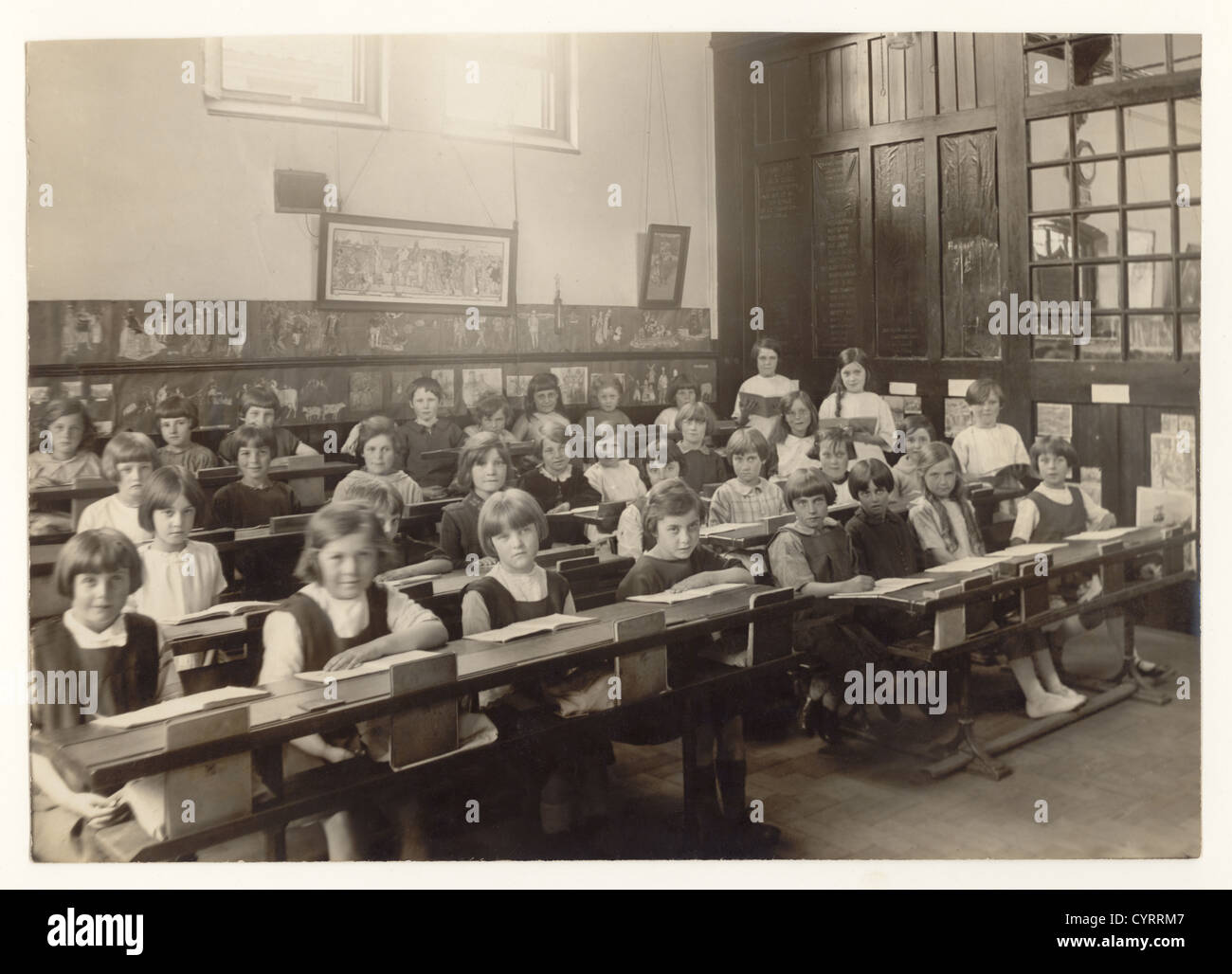 20's era vintage school photograph of junior girls in a classroom at a primary school, sitting at their desks with open books, circa 1925, U.K. Stock Photo