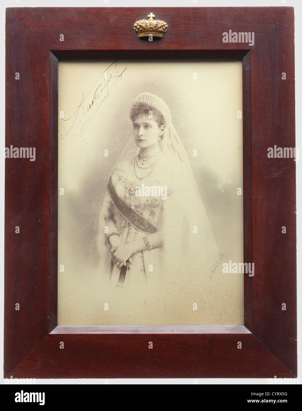 Portrait photo of Tsarina Alexandra Feodorovna, with handwritten signature in ink Russia, ca. 1900. The right edge with embossed signature of the court photographer 'A. Pasetti'. Printed in gold on the back the photographer's name with several medals. Slightly stained. Under glass, in brown lacquered wood frame, the top applied with a gold bronzed imperial crown of brass. The frame stand at back missing. Picture ca. 21.6 x 15 cm, frame 30.3 x 23.5 cm. Alexander Ivanovich Pasetti studied at the Saint Petersburg art academy and won silver medals there in 1872 and, Stock Photo