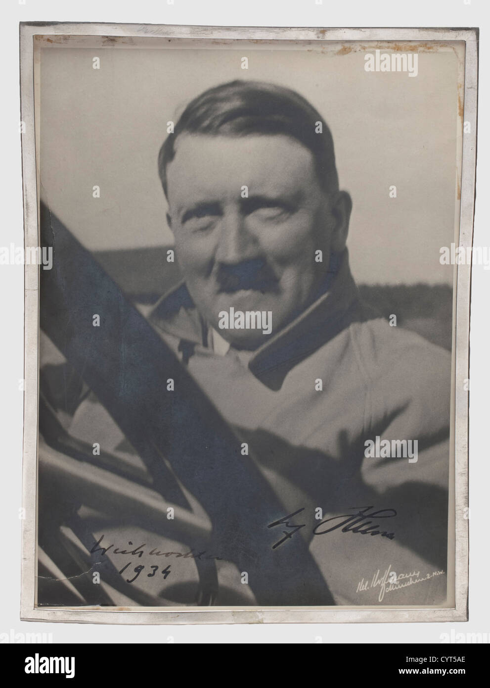 Adolf Hitler,a dedication photo 1934 Autograph signature and date in thick,black ink 'Weihnachten 1934 Adolf Hitler'(Christmas 1934 Adolf Hitler)on a large format Hoffmann photograph(dented on the lower edge)of Hitler in a coat sitting in the passenger's seat of an Mercedes convertible. The photographer's signature on the lower rim,'H. Hoffmann,München 2.N.W.' and the Hoffmann stamp on the back. Glued to the back piece of a simple,damaged(glass missing)tabletop frame. From the legacy of a high official of Daimler-Benz,historic,historical,people,1,Additional-Rights-Clearences-Not Available Stock Photo