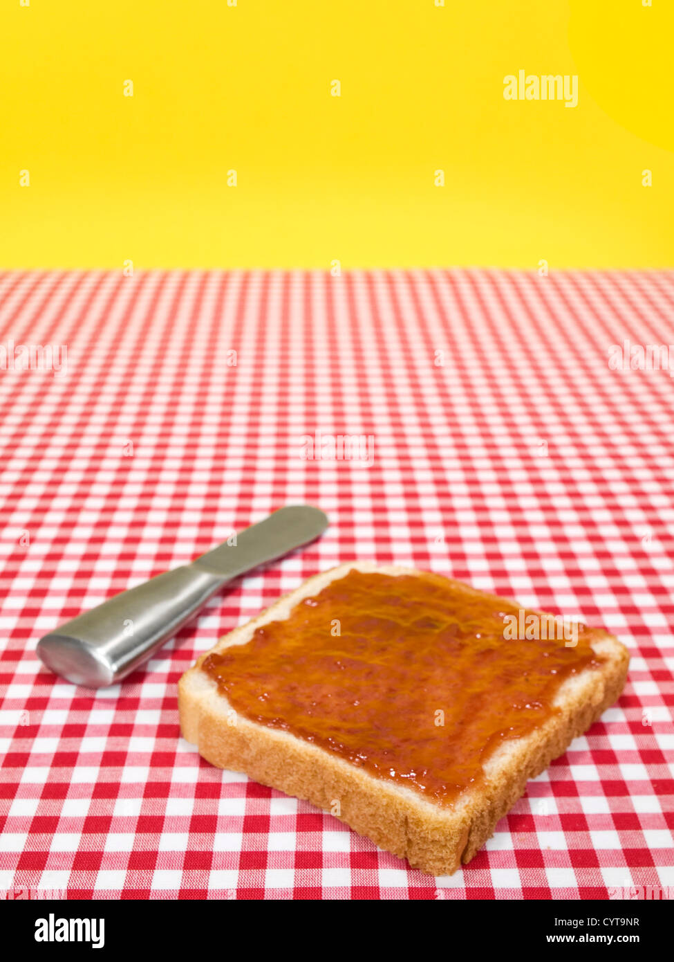 A slice of bread spread with jam and a knife over the table Stock Photo