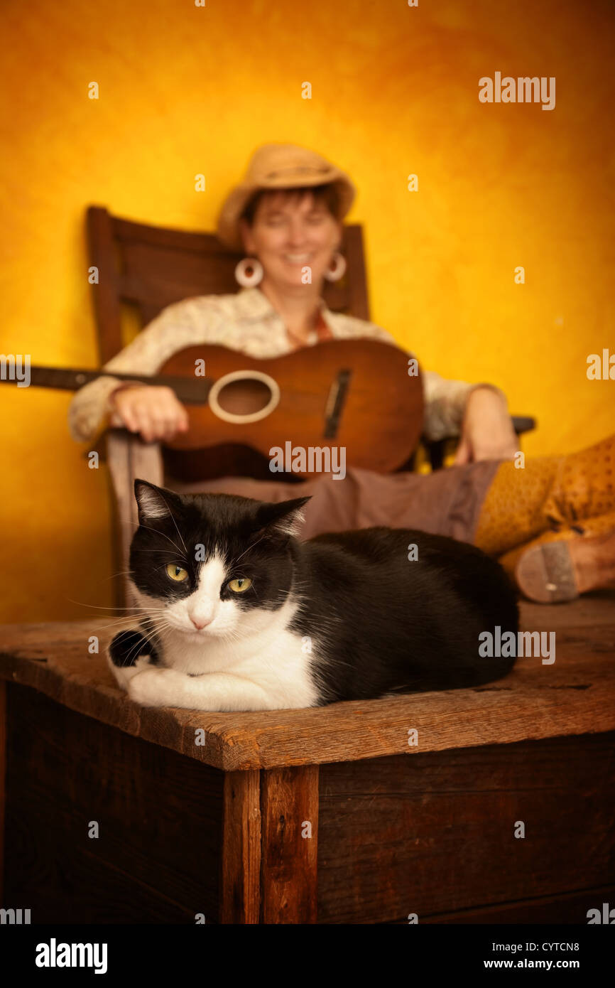 Pretty western woman in antique rocking chair with guitar and cat Stock Photo