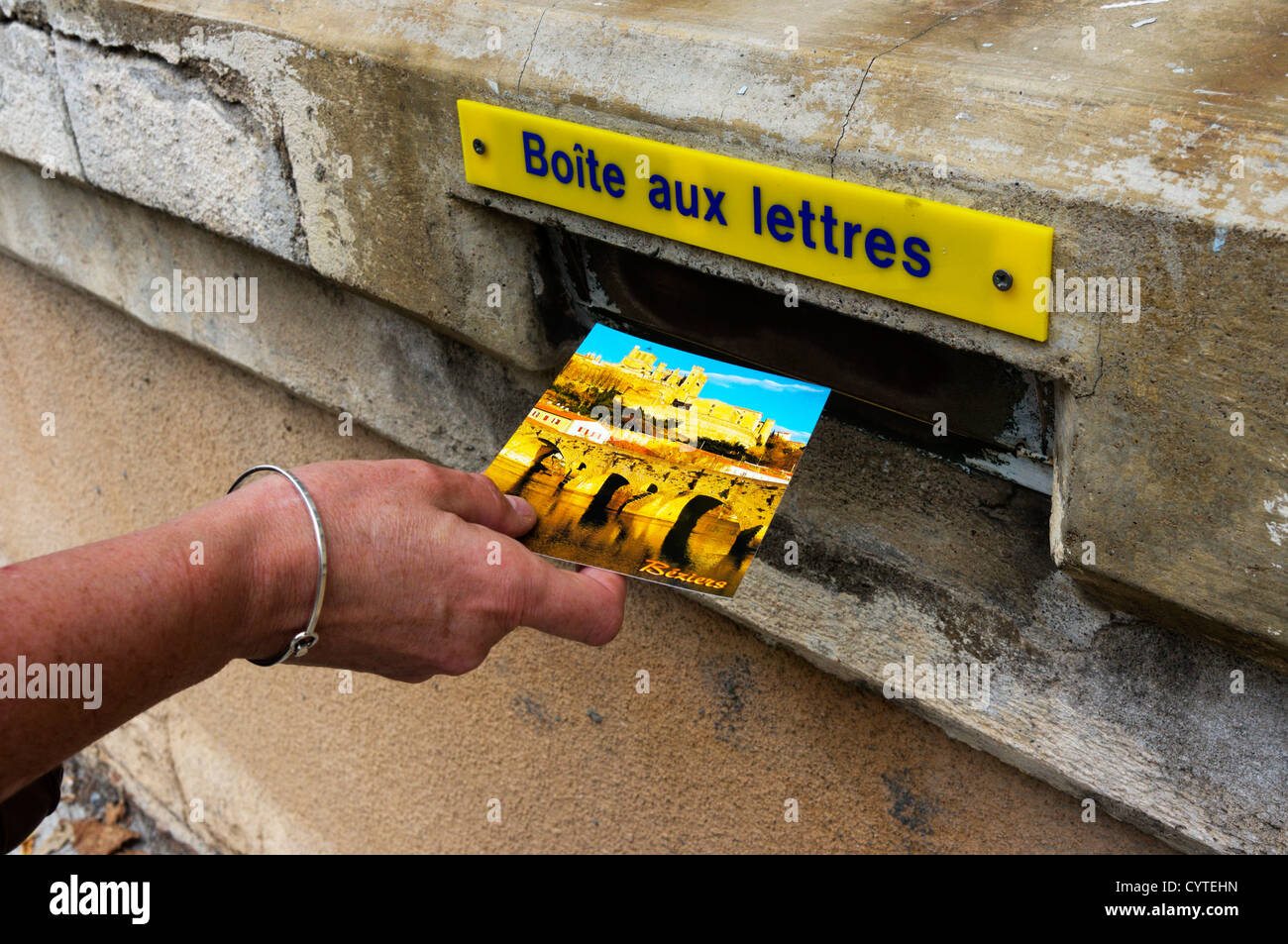 A female hand posts a postcard from Beziers in a French letterbox. Stock Photo