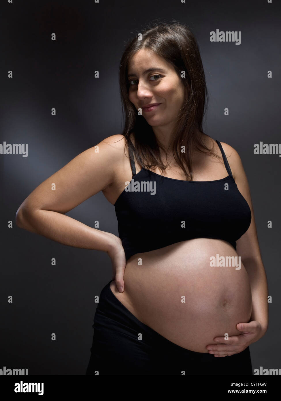 Pregnant woman holding her belly over a gray background Stock Photo - Alamy