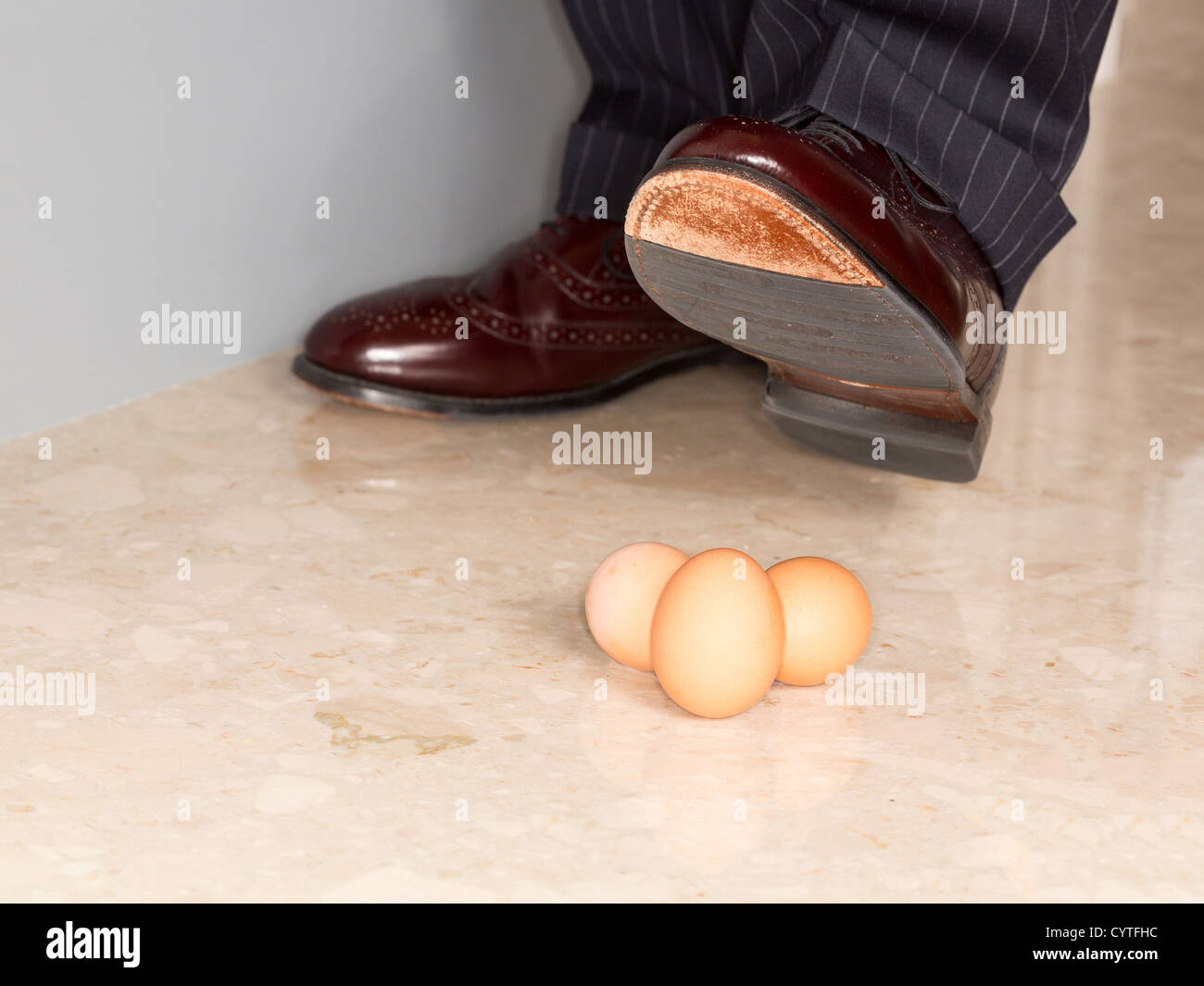 Male brown leather shoe in suit pants about to tread on three brown eggs Stock Photo