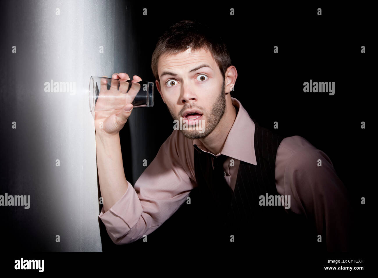 Handsome young man using glass against wall to eavesdrop Stock Photo