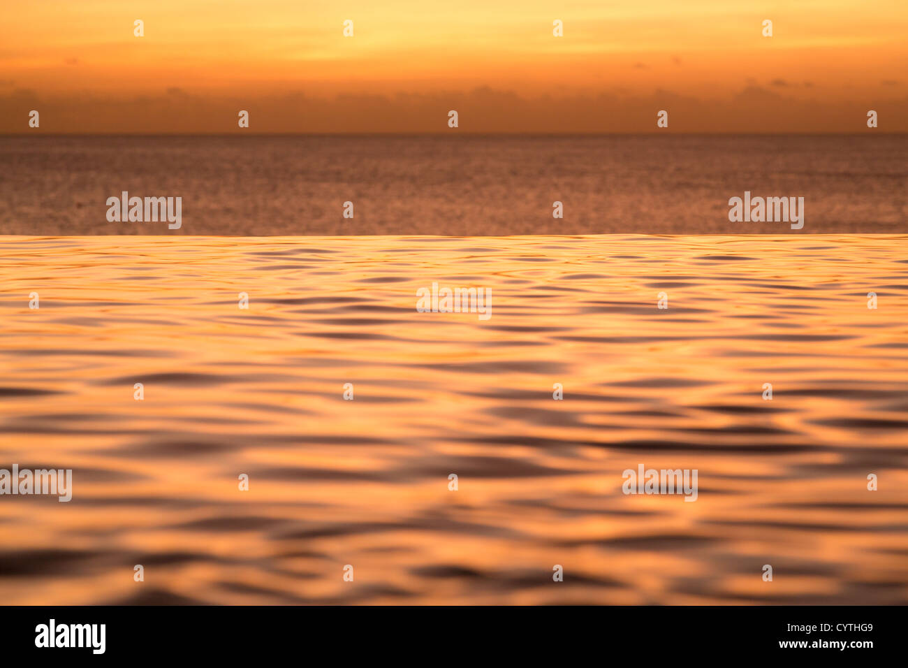Edge of infinity swimming pool overlooking ocean at sunset Stock Photo