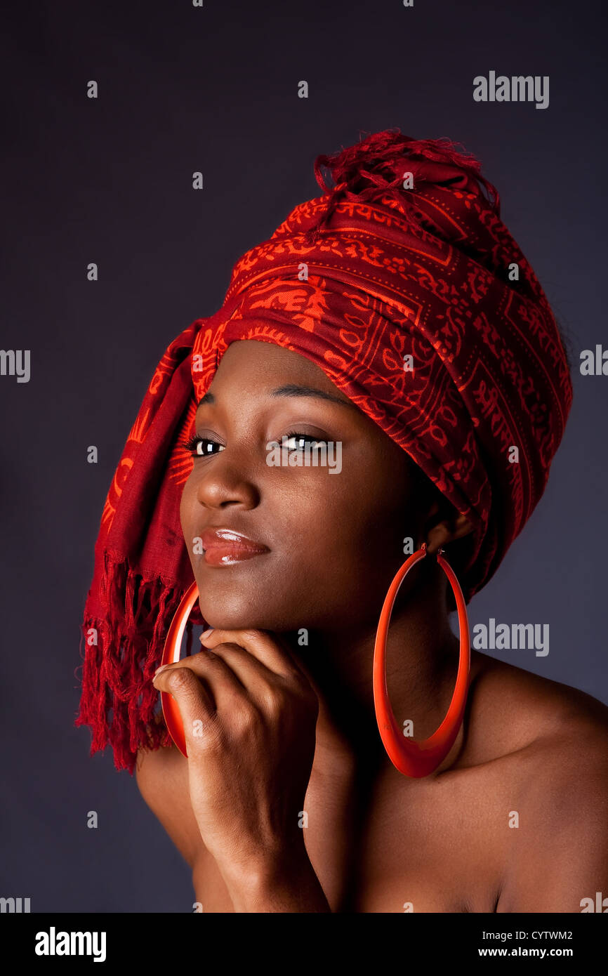 Beautiful African-American woman wearing a traditional tribal red orange head scarf and big orange hoop earrings, supporting her chin with hand, isolated. Stock Photo