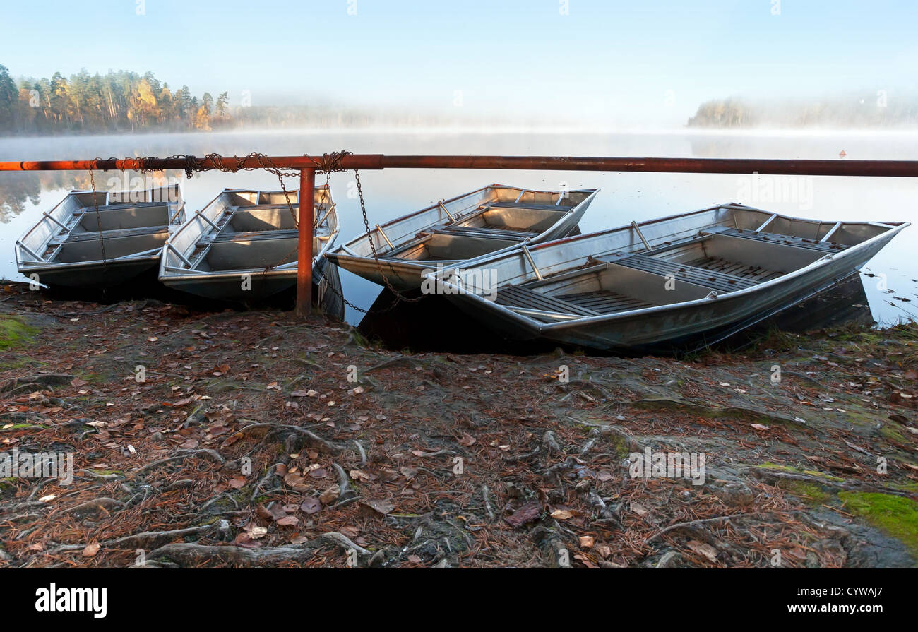Four small metal rowboats on still foggy lake coast in the morning Stock Photo