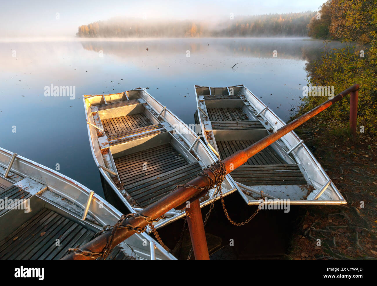 Small metal rowboats on still foggy lake coast in the morning Stock Photo