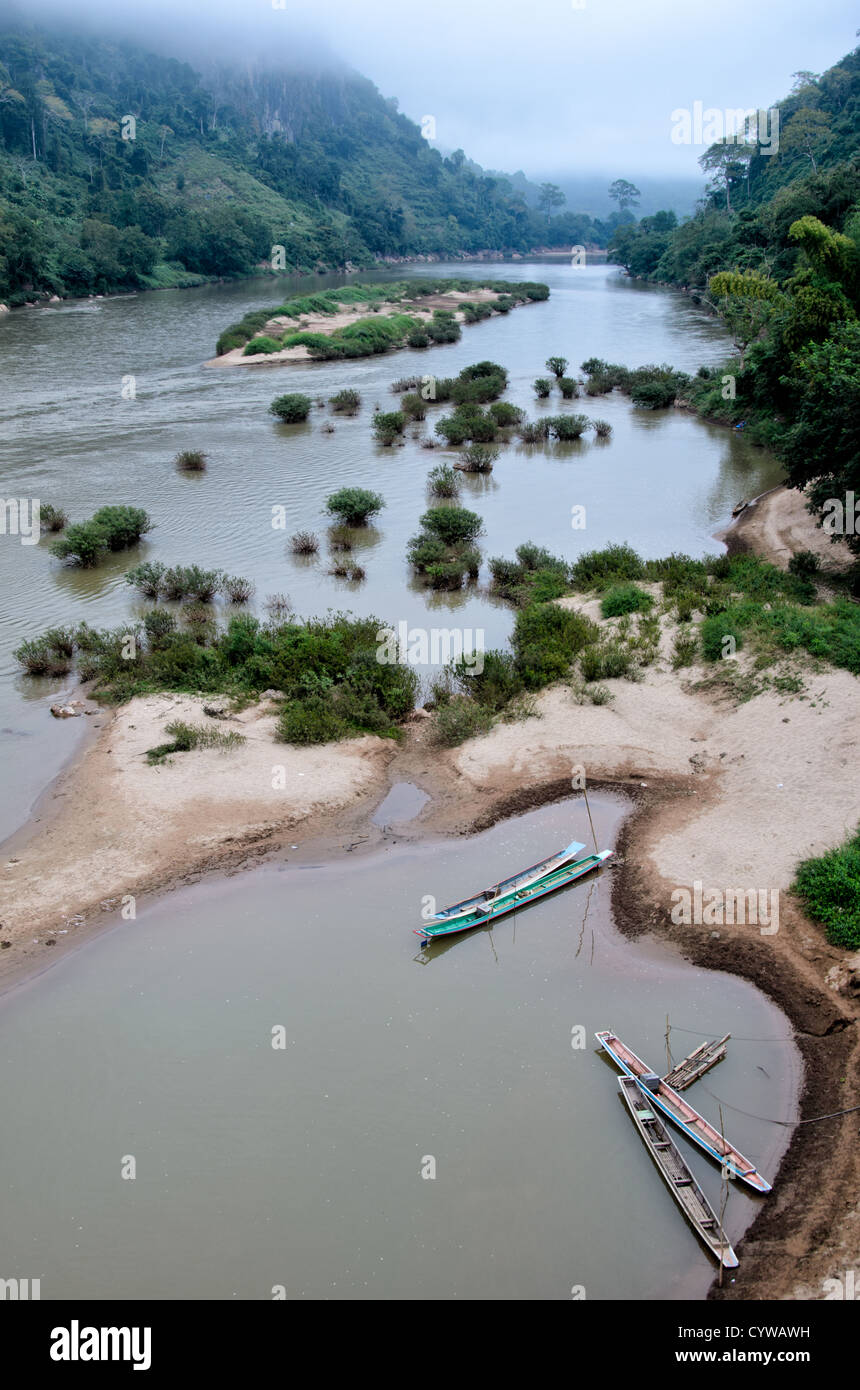 NONG KHIAW, Laos - In the foreground, wooden canoes are moored on riverbank of Nam Ou (River Ou) in Nong Khiaw in northern Laos. The sandy bottom of the river means that the current creates small, sandy islands and protected inlets on the river. Stock Photo