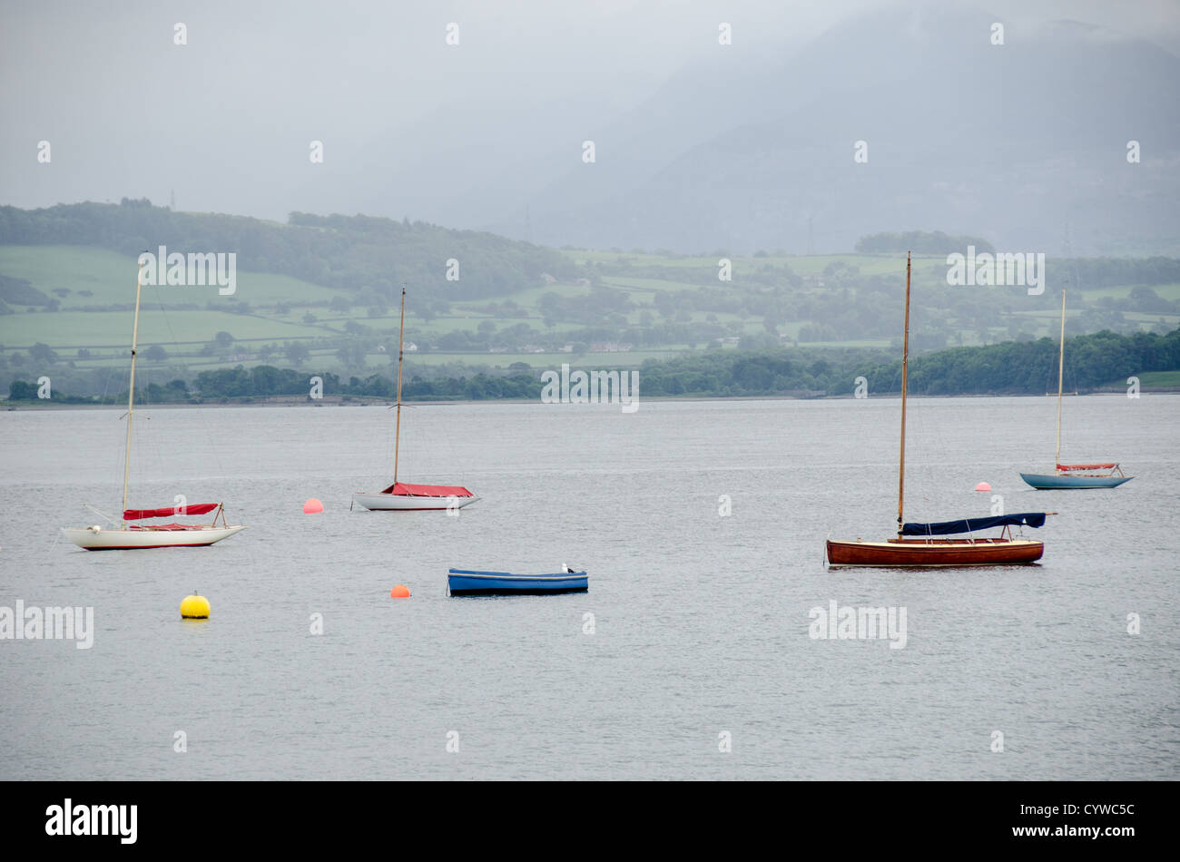 BEAUMARIS, Anglesey, Wales — Wooden sailboats moored on the calm waters of the Menai Strait near Beaumaris, on the island of Anglesey in north Wales. The boat is docked close to the town’s harbor, with scenic views of the Strait and the surrounding coastline, a popular spot for sailing and maritime activities. Stock Photo