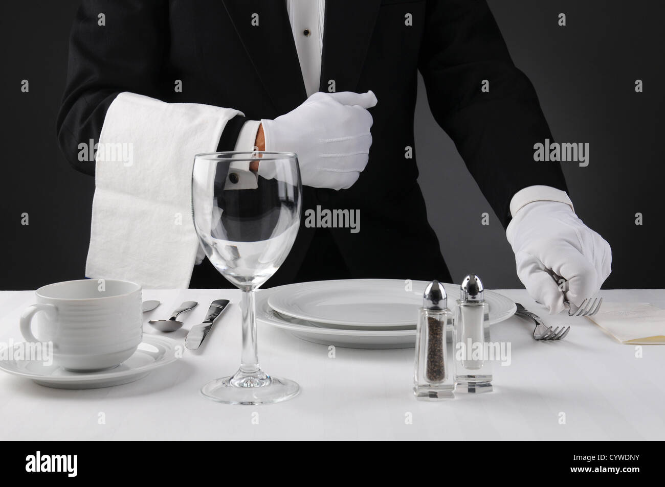 Closeup of a waiter in a tuxedo setting a formal dinner table. Shallow depth of field in horizontal format . Stock Photo