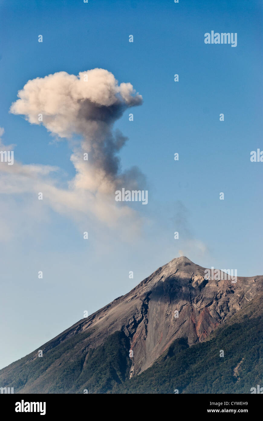 Volcán de Fuego emits a large puff of ash and smoke near Antigua Guatemala. Famous for its well-preserved Spanish baroque architecture as well as a number of ruins from earthquakes, Antigua Guatemala is a UNESCO World Heritage Site and former capital of Guatemala. Stock Photo
