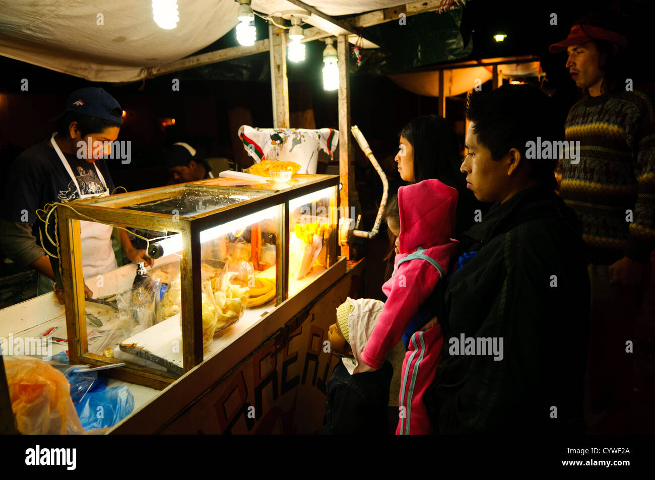 A family buys dinner at a street food vendor as part of a night market set up for the holiday of Our Lady of Guadalupe Day in Antigua, Guatemala. Stock Photo