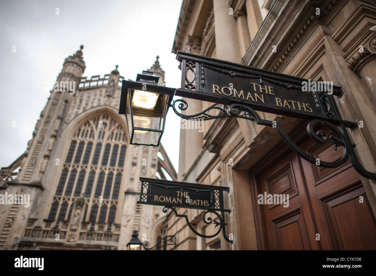 BATH, United Kingdom — The entrance to the historic Roman Baths, an ancient bathing and socializing complex built by the Romans around 70 AD, which gives the city of Bath its name. The well-preserved site features natural hot springs that have flowed for thousands of years, producing over one million liters of mineral-rich water daily. In the background stands the distinctive tower of Bath Abbey, a Gothic church completed in the 16th century on the site of earlier religious buildings. Both the Roman Baths and Bath Abbey are central landmarks in the UNESCO World Heritage city of Bath in Somerse Stock Photo