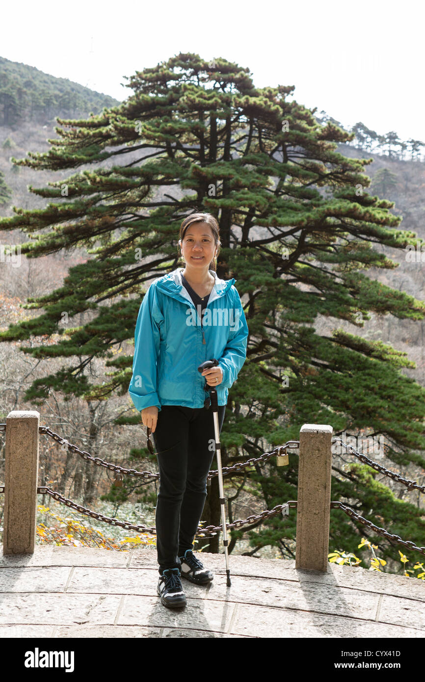 Asian women hiking in Yellow Mountains with large tree and mountains in background Stock Photo