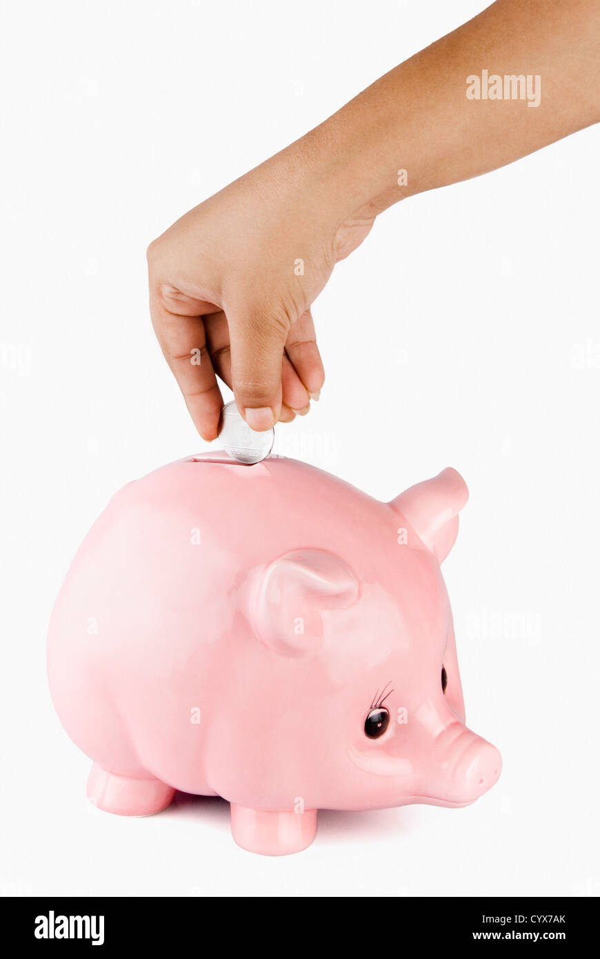 Close-up of a person's hand putting a coin into a piggy bank Stock Photo