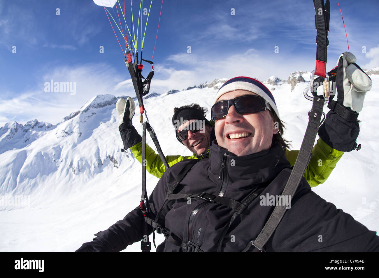 Two people hanging under a paraglider ove the mountain tops of the Swiss alps. They enjoy a stunning view over the white rocks Stock Photo
