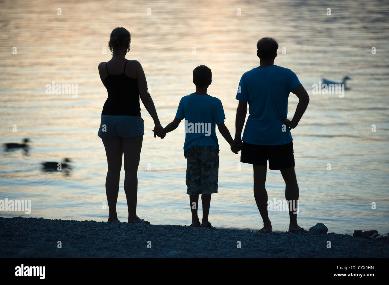A happy family staring over the water during sunset while they hold each other hands Stock Photo