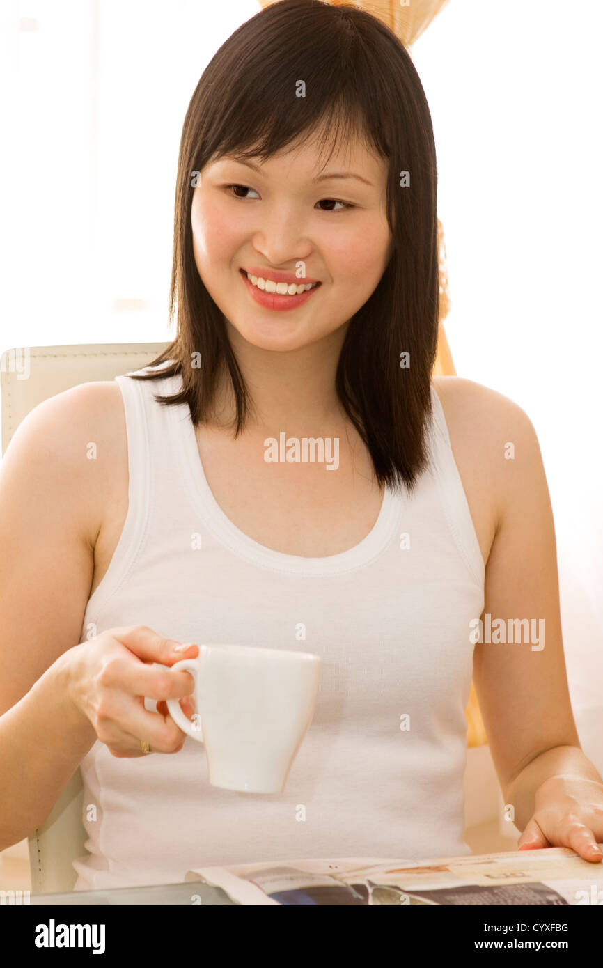 A beautiful young Asian woman drinking tea and reading newspaper. Stock Photo