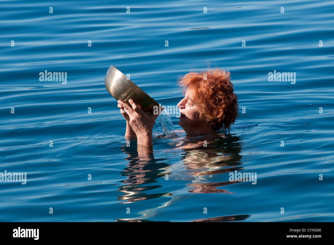 Woman pouring out water from a Tibetan singing bowl in the sea Stock Photo