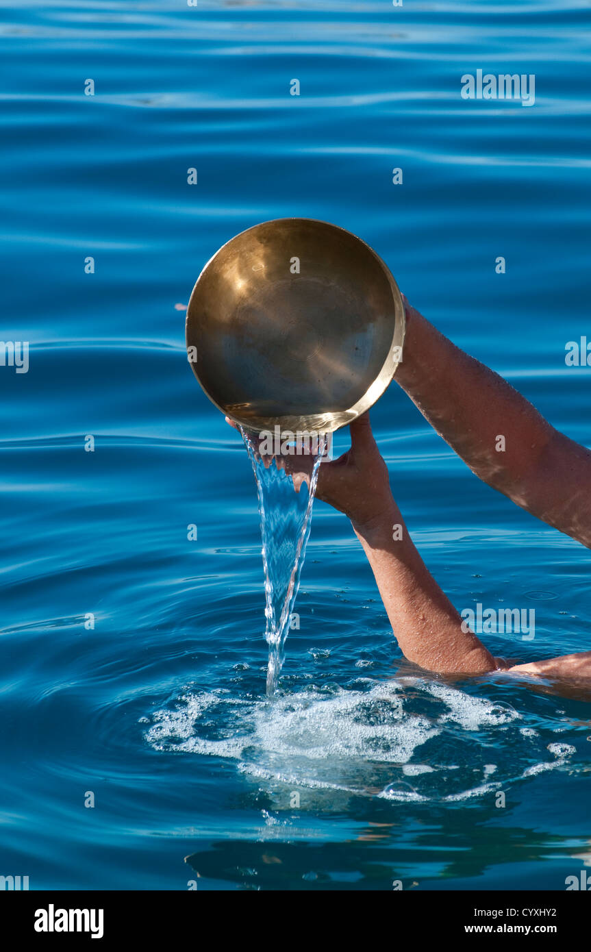Hands pouring out water from a Tibetan singing bowl in the sea Stock Photo