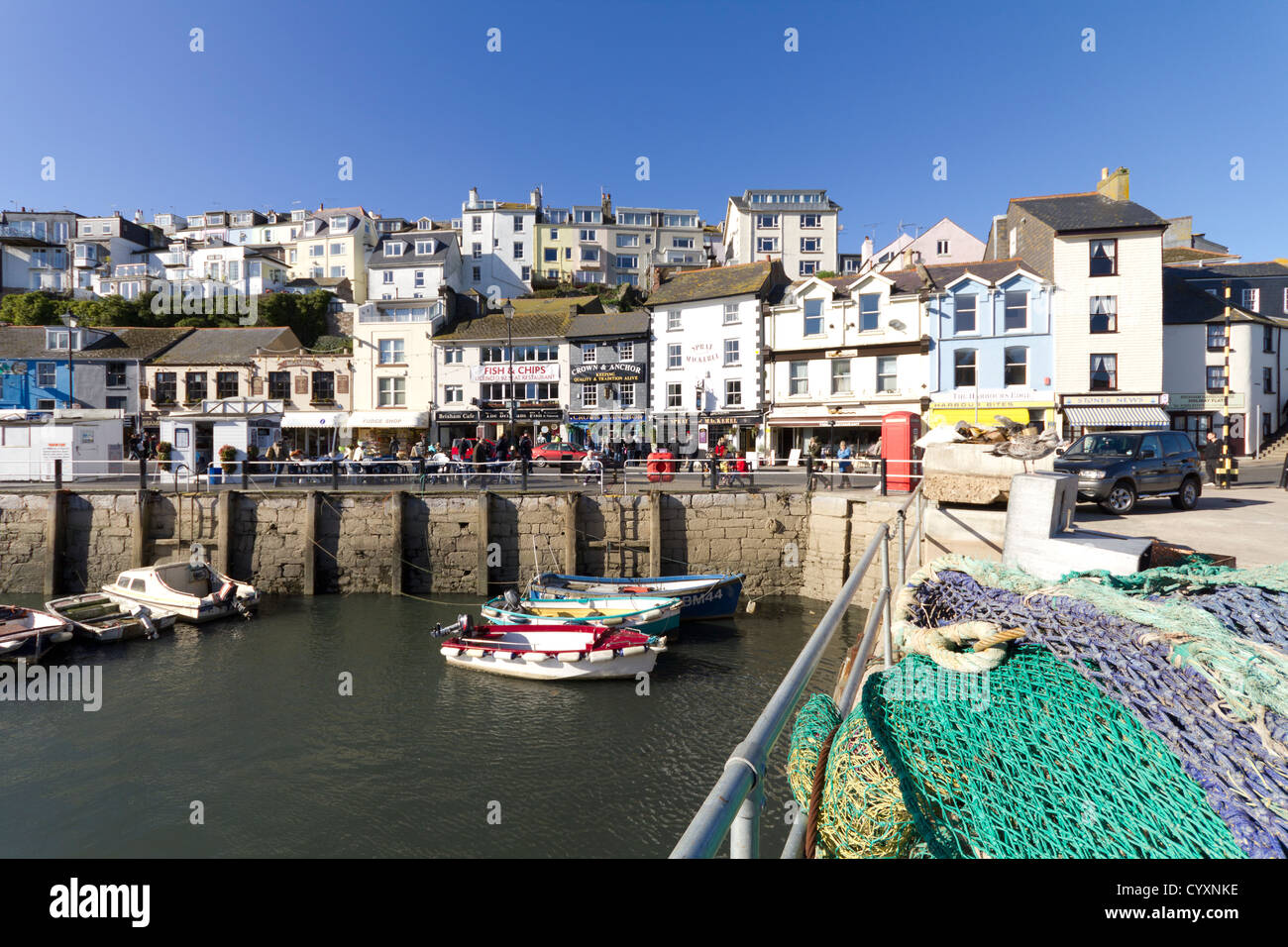 The two sides of Brixham in Devon, UK. Fishing nets lie on the quayside, next to small fishing boats and pleasure craft. Stock Photo
