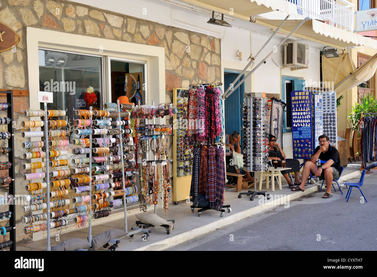 Quiet shopping street in town of Kardamena, Kos island, Greece, with shop owners relaxing outside tourist shop. Stock Photo