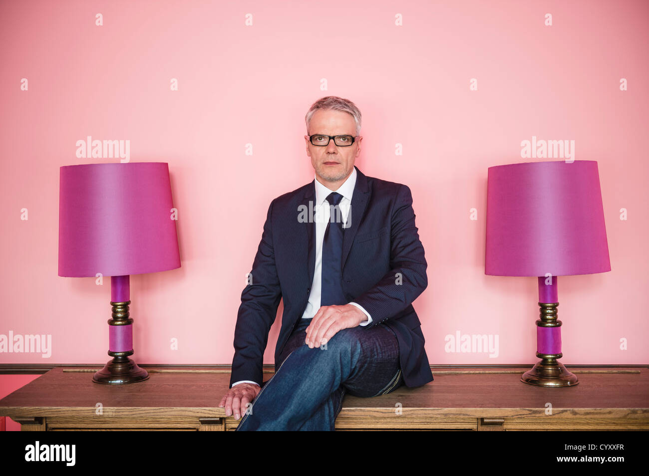 Germany, Stuttgart, Businessman sitting on sideboard with lamps, smiling, portrait Stock Photo