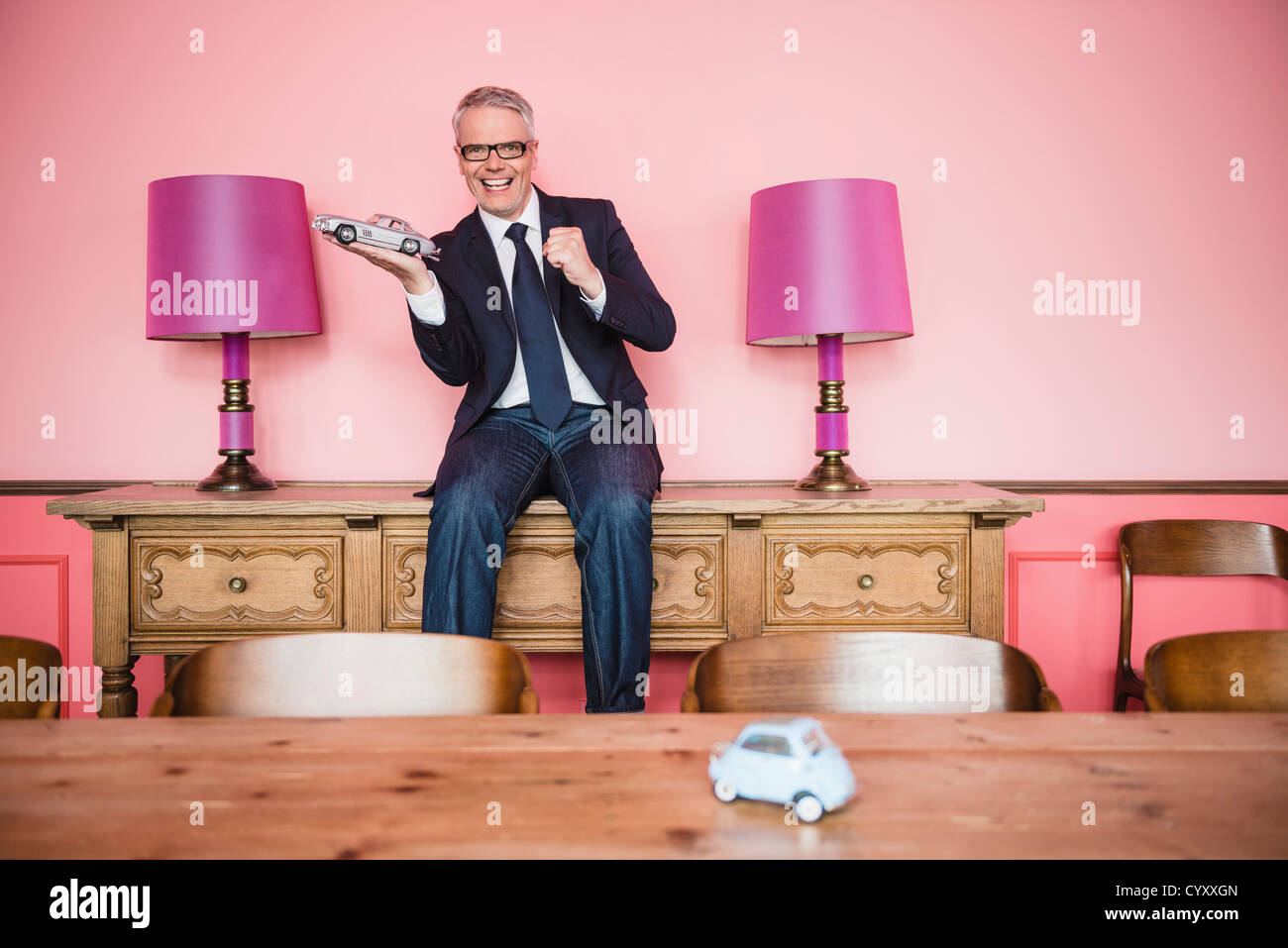 Germany, Stuttgart, Businessman sitting on sideboard with toy car, smiling, portrait Stock Photo