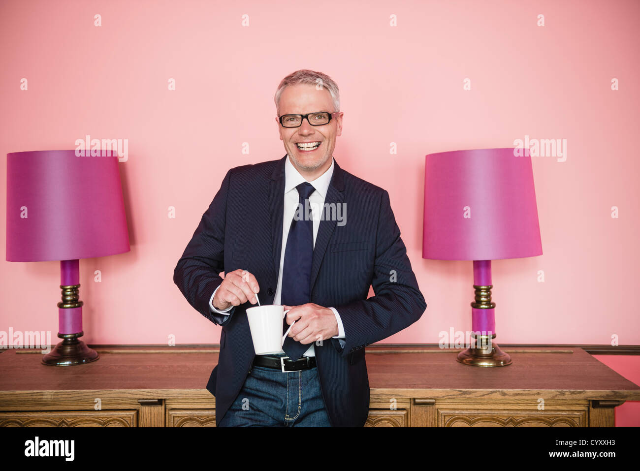 Germany, Stuttgart, Businessman stirring in cup, smiling, portrait Stock Photo