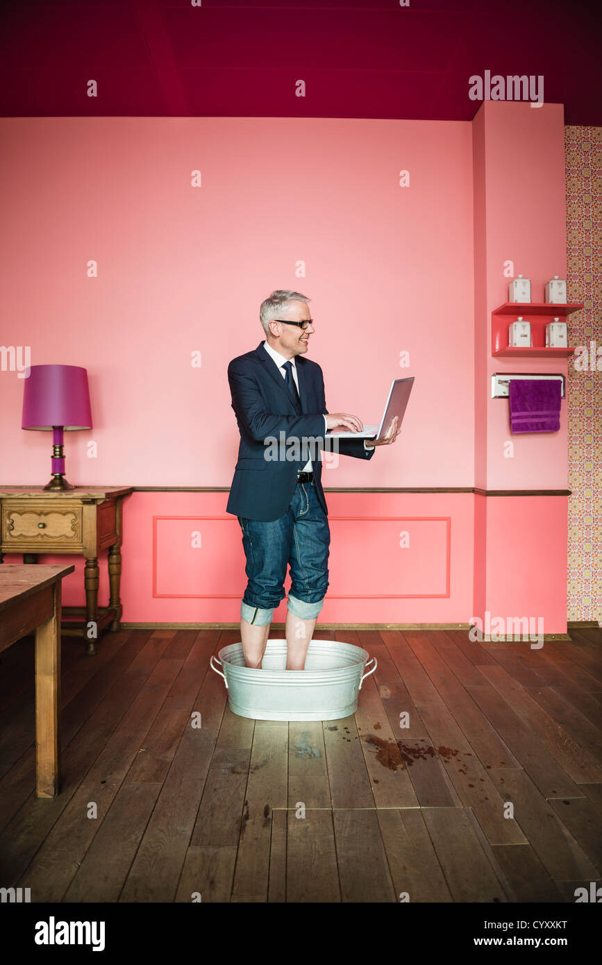 Germany, Stuttgart, Businessman standing in bathtub and using laptop Stock Photo