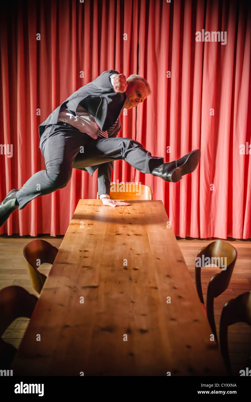 Germany, Stuttgart, Businessman jumping over table in apartment Stock Photo Alamy
