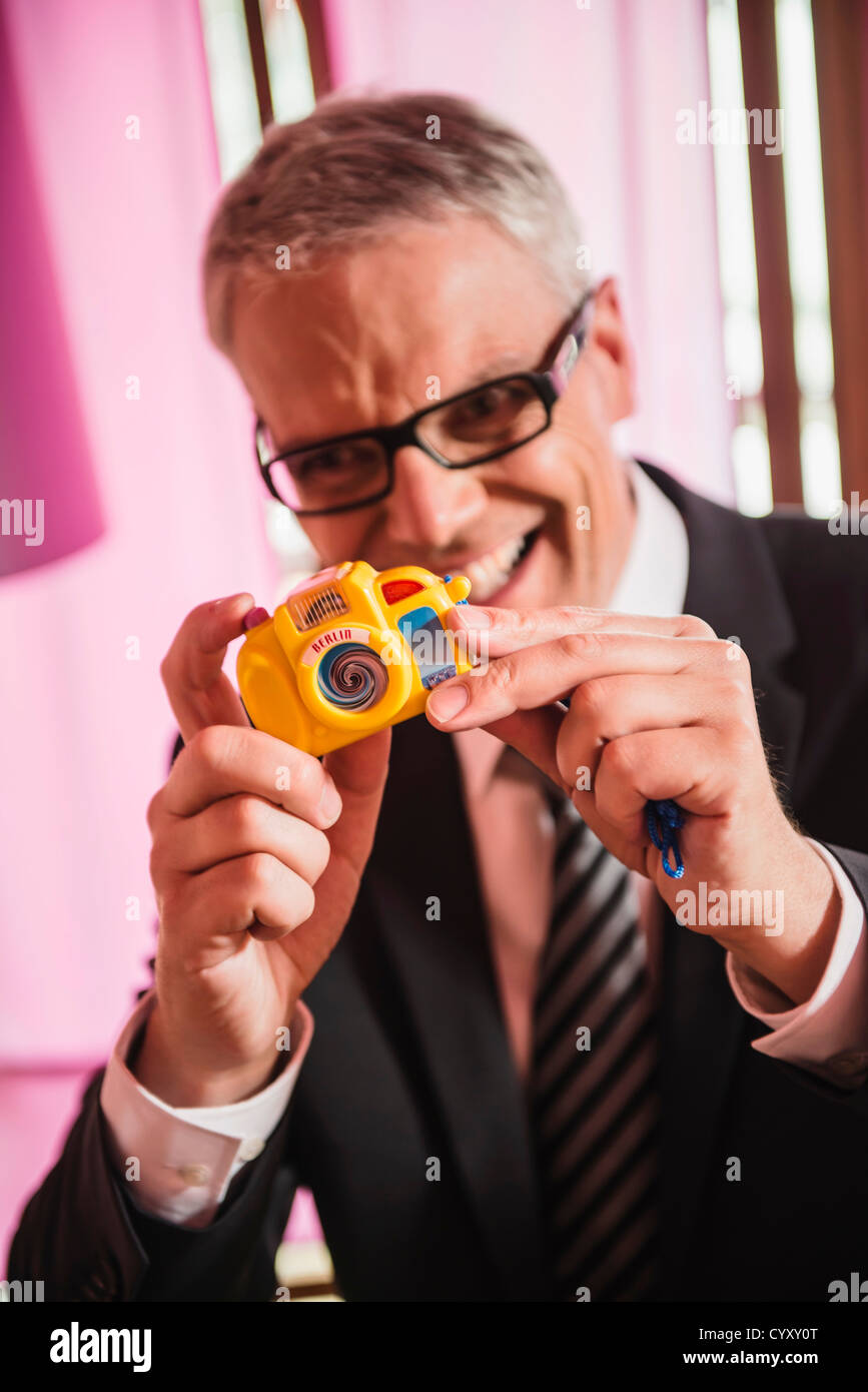 Germany, Stuttgart, Businessman photographing with toy camera, smiling Stock Photo