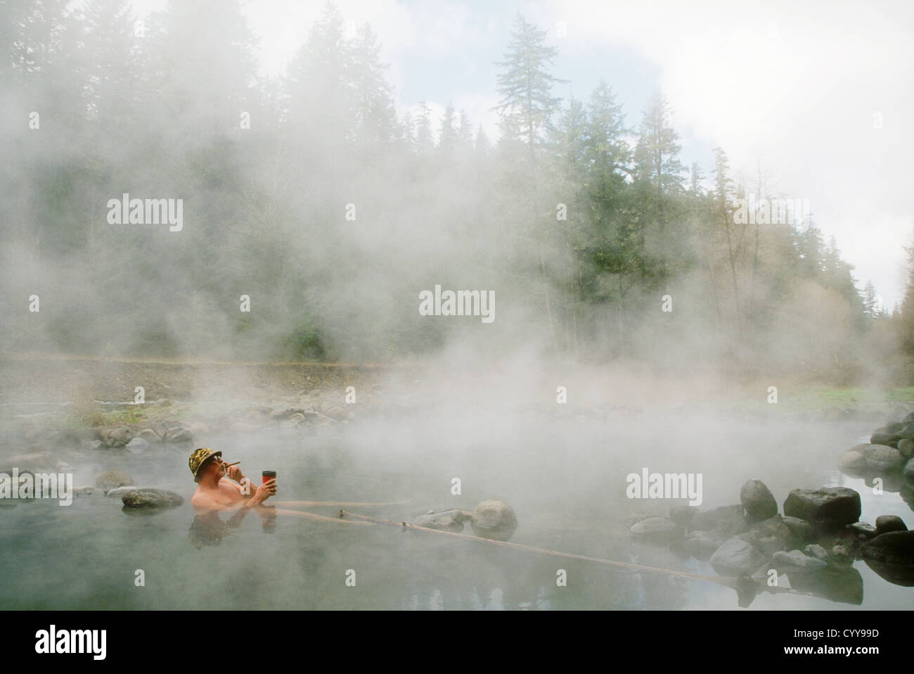Man with cigar & coffee soaking in pool at McCredie Hot Springs along Salt Creek; Willamette National Forest, Oregon. Stock Photo
