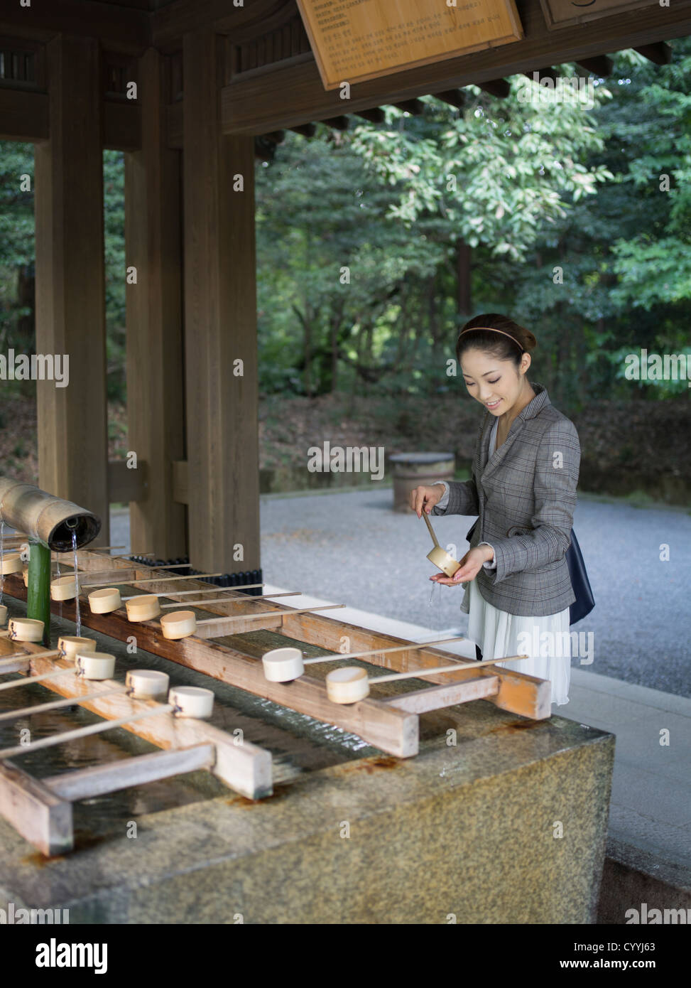 Beautiful young Japanese woman visiting Meiji Jingu Shrine, Tokyo At the purification trough (chōzuya or temizuya) Stock Photo