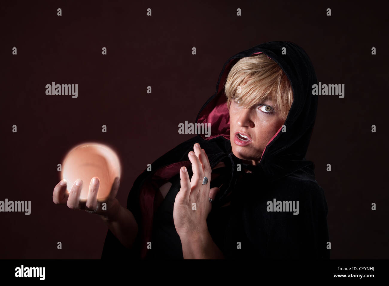 Caucasian female fortuneteller wearing black viel holds crystal ball over maroon background Stock Photo