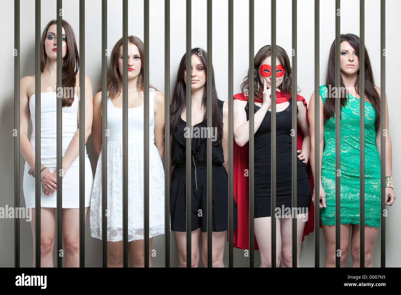 Woman in superhero costume with female friends standing behinds prison bars Stock Photo