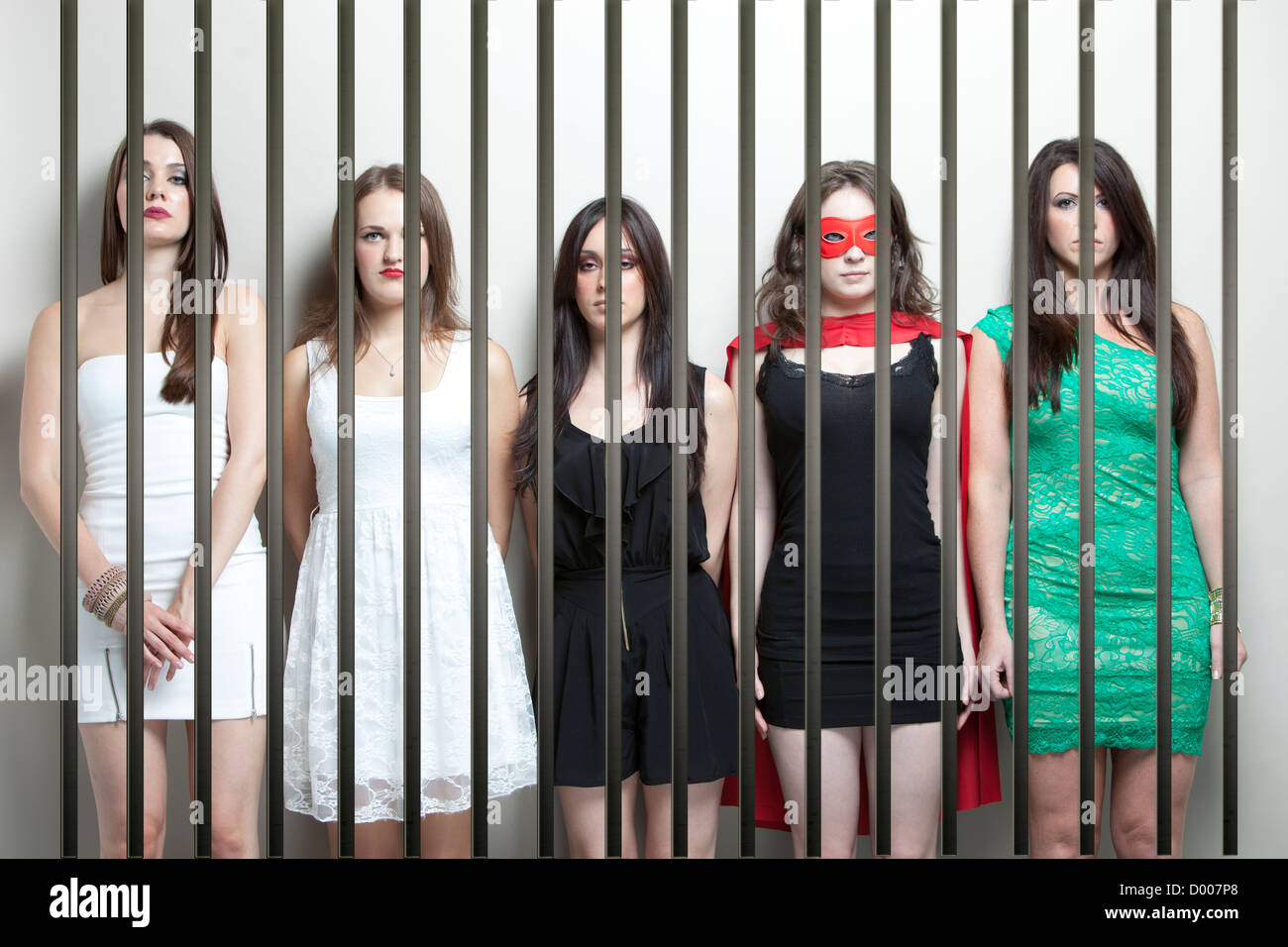 Woman in superhero costume with female friends standing behinds prison bars Stock Photo