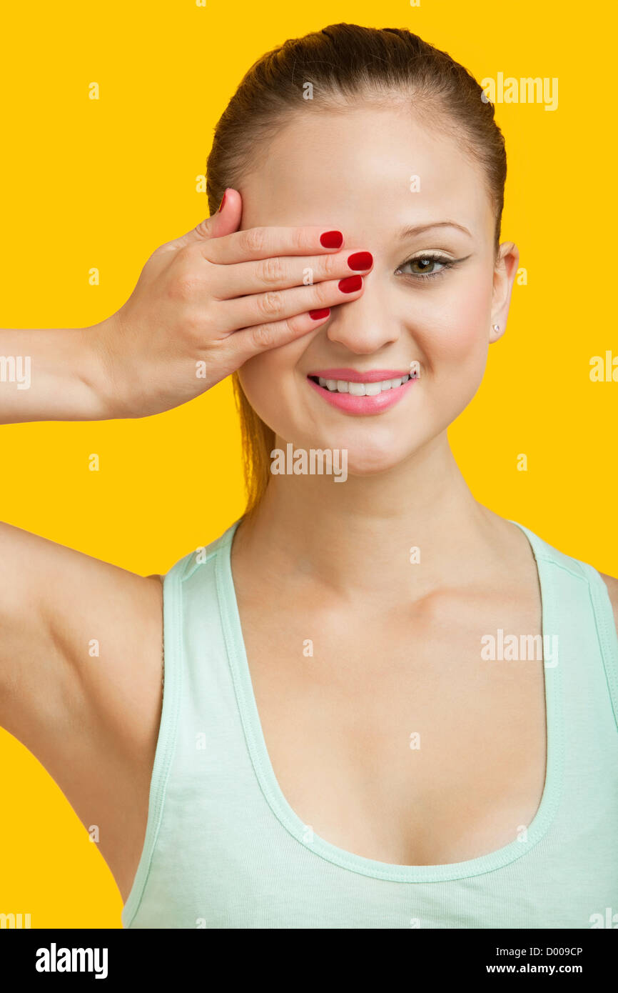 Portrait of a beautiful young woman covering eye over yellow background ...