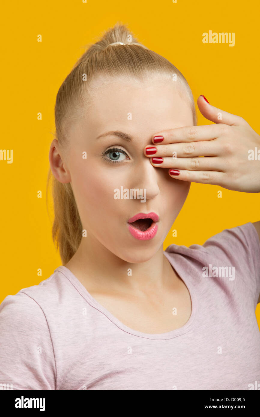 Portrait of a beautiful young woman covering eye over yellow background ...