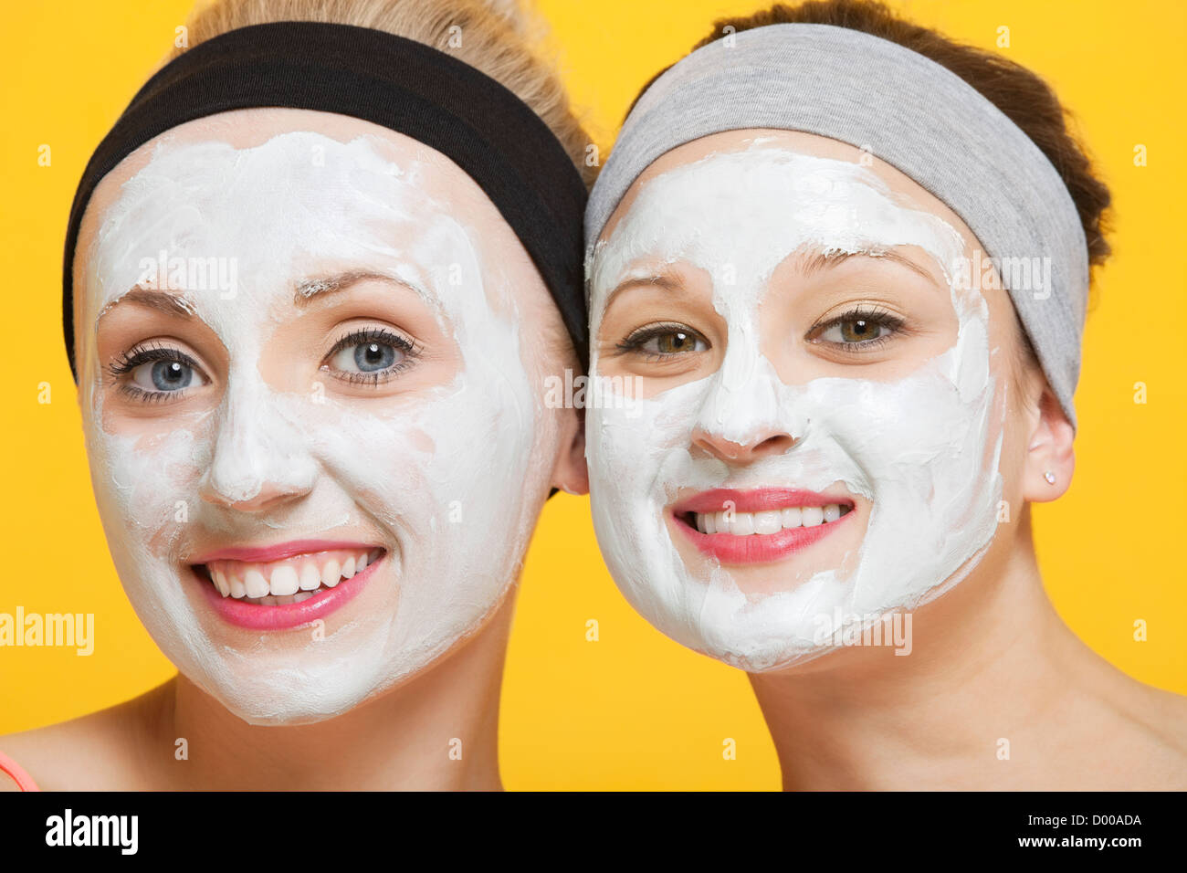Portrait of two happy women with face pack on their faces over yellow background Stock Photo