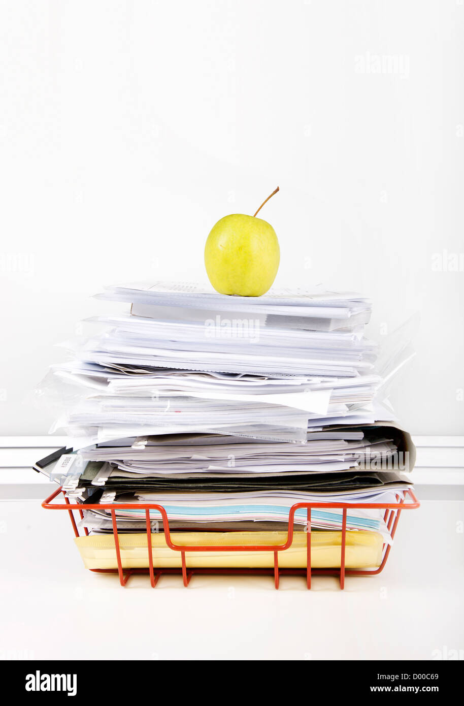 Granny smith apple on stack of documents in desk tray against white wall Stock Photo
