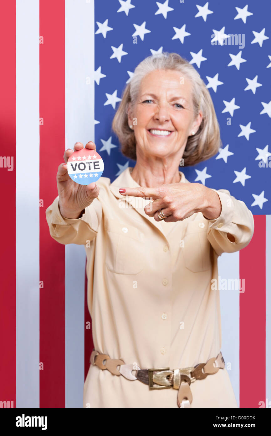 Portrait of senior woman pointing at election badge against American ...