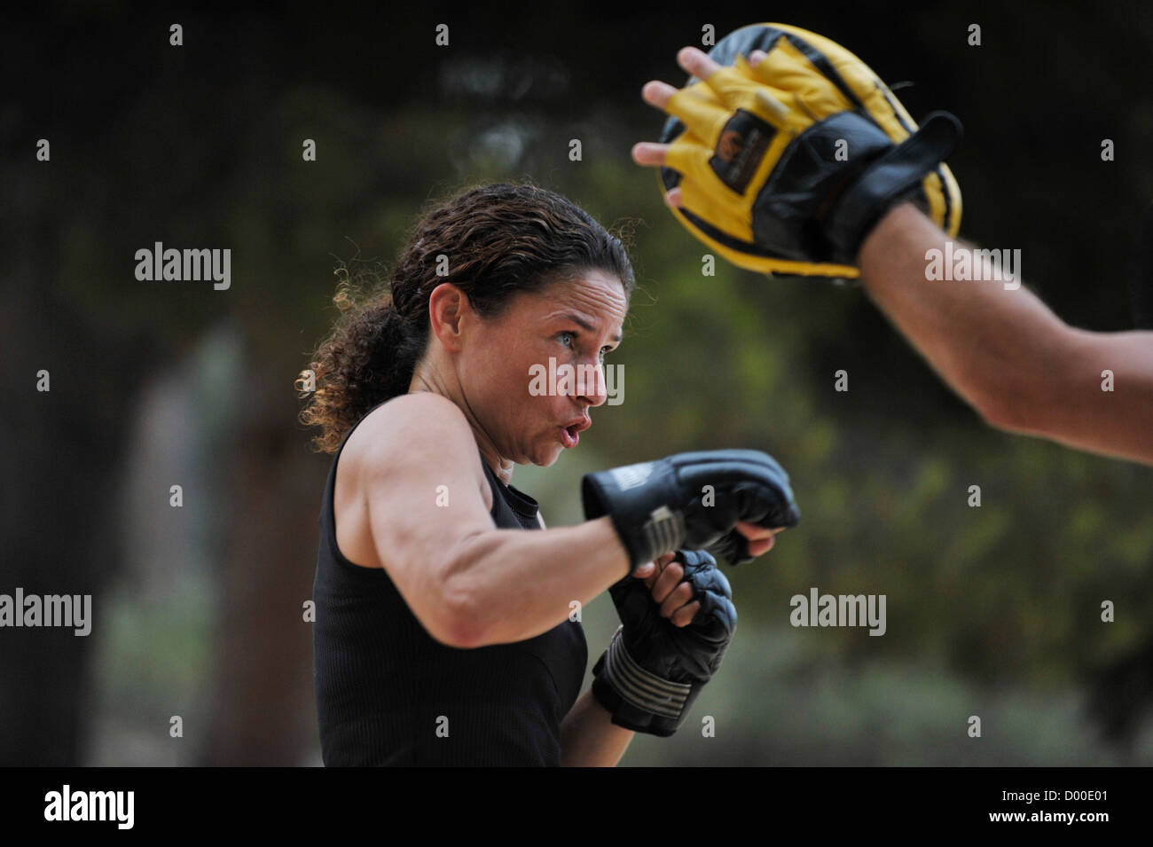 woman in her forties strikes boxer pose and watches padded hand during martial arts training in a park Stock Photo