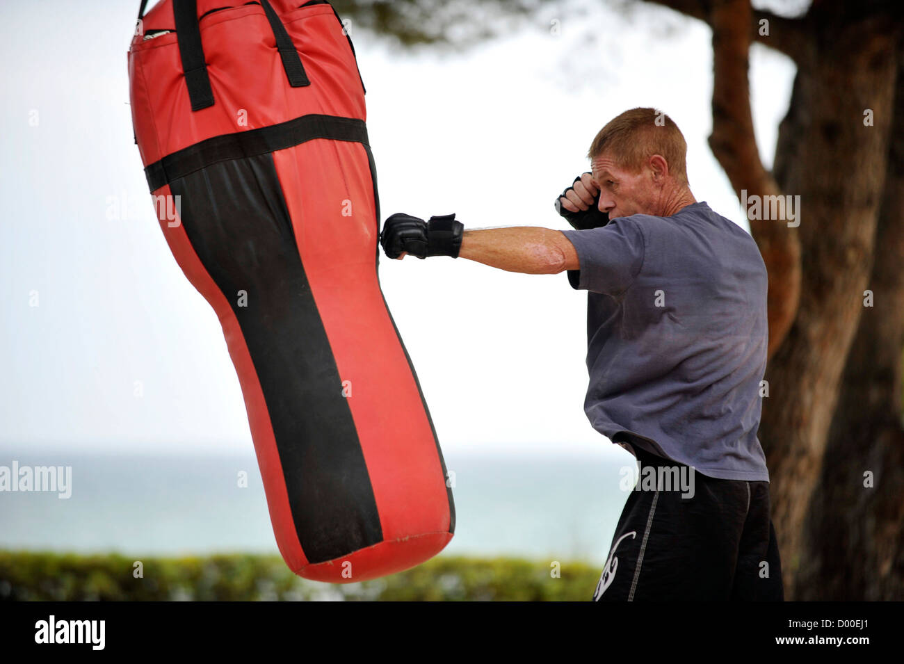 man in hist forties trains boxing hits on sandbag in park near the Sea outside Stock Photo